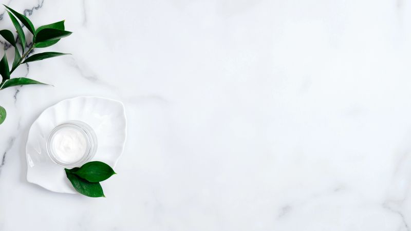 Natural organic moisturizing cosmetic cream with green leaves on marble table