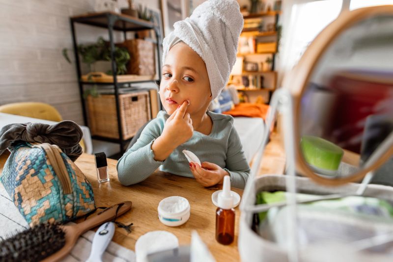 Smiling little girl with towel twisted around head applying skin cream