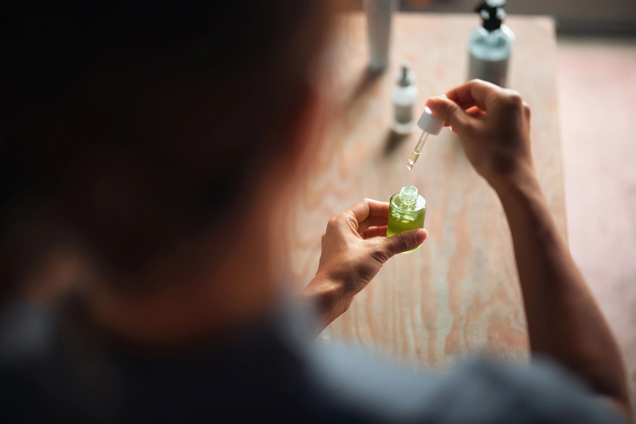 Close-up of a person using a dropper to extract green liquid from a bottle
