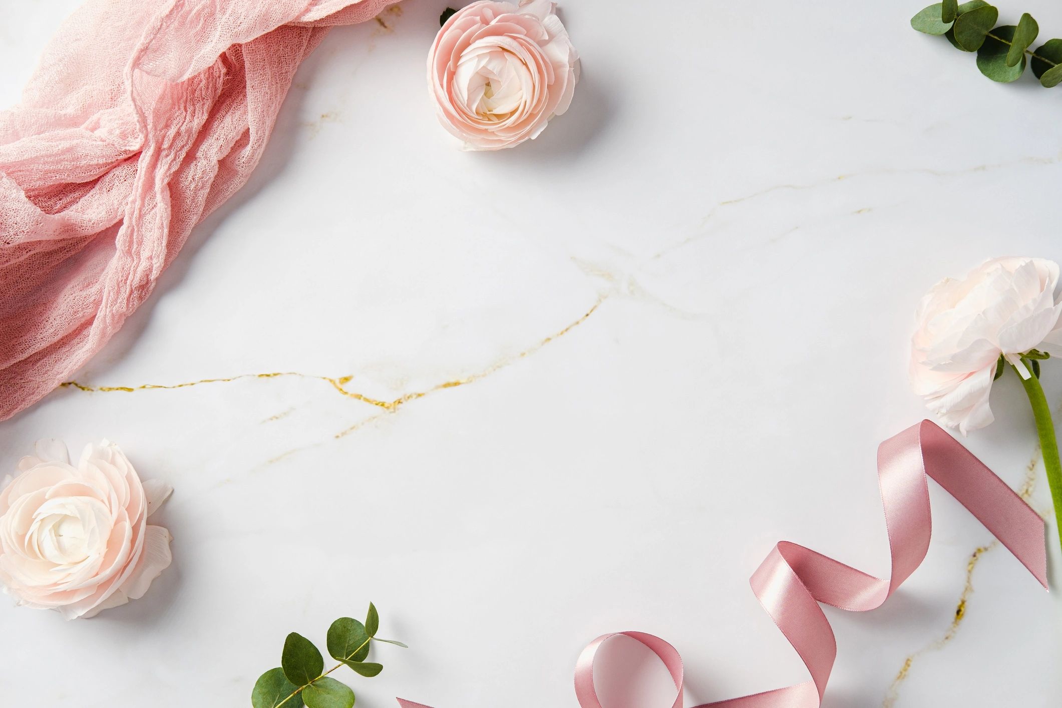 Soft pink roses, eucalyptus leaves, fabric, and ribbon styled on marble